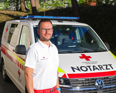Das Bild zeigt den langjährigen Notfallsanitäter Markus der Rotkreuz-Bezirksstelle Graz-Stadt vor einem Notarzteinsatzfahrzeug.