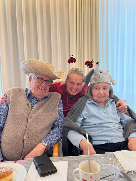 Eine Pflegemitarbeiterin umarmt von hinten zwei verkleidete Bewohnerinnen.