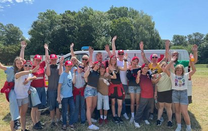 eine Gruppe von Kindern, Jugendlichen und Jugend-Betreuer:innen steht vor einem Bus und lächeln in die Kamera zum Abshcluss des Lagers