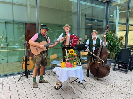 Ein Musiktrio bestehend aus einem Gitarristen, einem Ziehharmonikaspieler und einem Kontrabassisten, alle in Tracht
