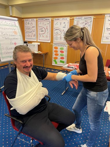 Eine Frau legt einem Mann einen Verband am Unterarm an.