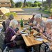 Bewohnerinnen und Bewohner sitzen an Tischen und genießen Essen und Getränke während des Grillfestes