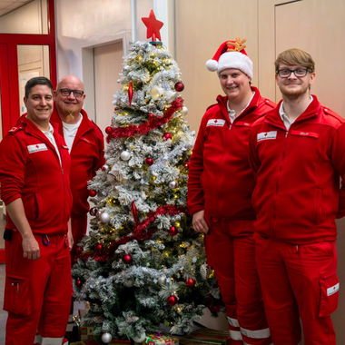 Vier Rotkreuz-Mitarbeiter in Uniform bei einem festlich geschmückten Christbaum.
