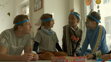 Kinder spielen mit Freiwilligem ein Gesellschaftsspiel im Rotkreuz-Lernhaus