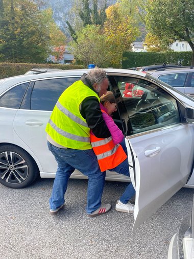 Ein Mann in Warnweste zieht eine verletzte Person über die offene Beifahrertür aus einem Auto.