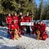 Gruppenfoto mit Mitgliedern der Suchhunde-Staffel des Roten Kreuzes Salzburg. Fünf Hunderführerinnen stehen und halten eine Tafel mit der Aufschrift "Wir sind da" in der Hand, davor knien drei Hundeführer, zwei davon mit Suchhund. Einer hält eine Lawinenschaufel in der Hand.