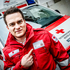 Zivildiener steht in Uniform vor Rettungsauto und deutet auf seinen Zivildienstausweis