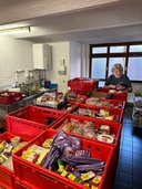 TÖT Aktionstag 2026 - © Österreichisches Rotes Kreuz / LV Oberösterreich Mehrere rote Kunststoffkisten mit haltbaren Lebensmitteln in einem Raum mit Fliesenboden und einem Fenster, eine Person steht im Hintergrund und sortiert Lebensmittel.