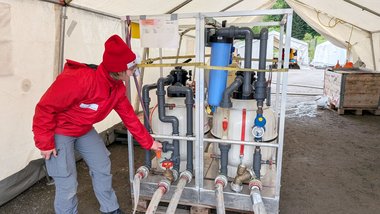 Eine Frau in Rotkreuz-Jacke bedient eine Filtrations-Anlage