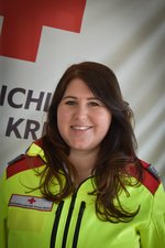Frau Michaela Scheiber in Rotkreuz-Uniform vor einer Rotkreuz-Standarte.