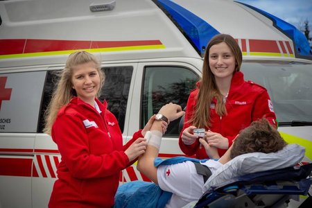 Zwei weibliche Sanitäterinnen vor einem Rettungsauto wie sie einen Patienten betreuen.