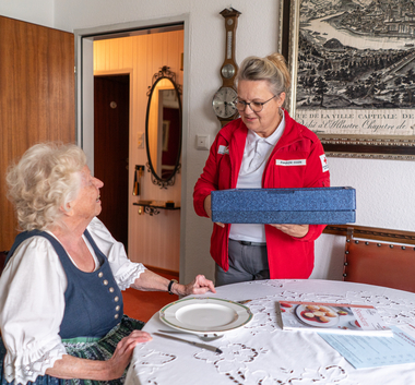 Eine Zuhause-Essen-Mitarbeiterin liefert eine Essenspaket an eine Klientin