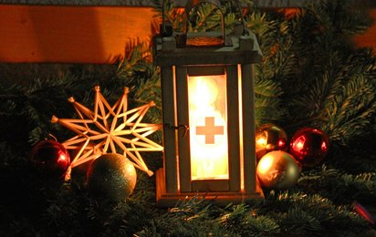 Friedenslicht mit Holzstern vor Tannenzweigen