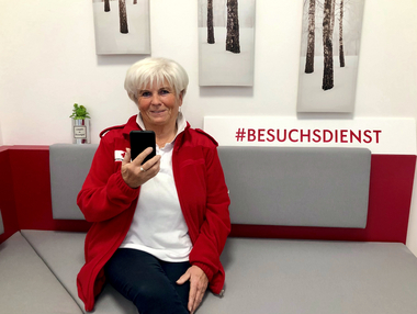 Besuchsdienst-Mitarbeiterin sitzt mit dem Handy in der Hand