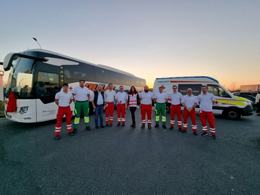 Eine Gruppe von Rotkreuz-Mitarbeiter:innen steht vor einem Bus und einem Rettungswagen.