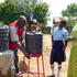 Eine Rotkreuz-Helferin in Uganda unterstützt bei einem Wasserprojekt. Ein lokaler Rotkreuz-Helfer wäscht sich die Hände unter einem Kanister, weitere Personen schauen zu.