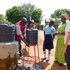 Eine Rotkreuz-Helferin in Uganda unterstützt bei einem Wasserprojekt. Ein lokaler Rotkreuz-Helfer wäscht sich die Hände unter einem Kanister, weitere Personen schauen zu.
