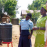 Eine Rotkreuz-Helferin in Uganda unterstützt bei einem Wasserprojekt. Ein lokaler Rotkreuz-Helfer wäscht sich die Hände unter einem Kanister, weitere Personen schauen zu.