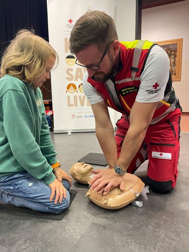 Ein Notarzt erklärt einem Schüler mittels einer Trainingspuppe wie die Herzmassage funktioniert.