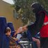 Eine Mitarbeiterin des IFRC reicht einer Frau mit einem Kind auf ihrem Arm einen Becher Wasser