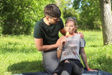 Ein Mann und eine Frau sitzen auf einer Picknickdecke. Sie lutscht ein Eis.