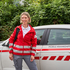 Marianne Zimmerebner, Leiterin der Mobilen Krankenpflege, in Rotkreuz-Jacke und mit Rucksack vor einem Rotkreuz-Fahrzeug