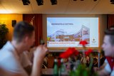 Bildschirm mit der Präsentation bei der Generalversammlung 2024. Die Gäste sitzen im Vordergrund