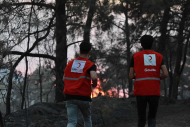 Zwei Helfer des Türkischen Roten Halbmonds laufen auf die Flammen zu