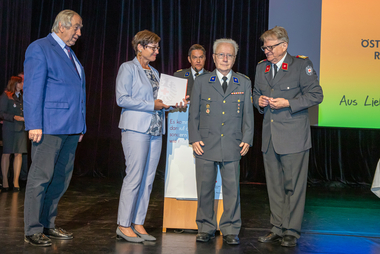 Gruppenbild mit 5 Personen, 1 Frau, 4 Männer, eine Person wird ein Abzeichen verliehen