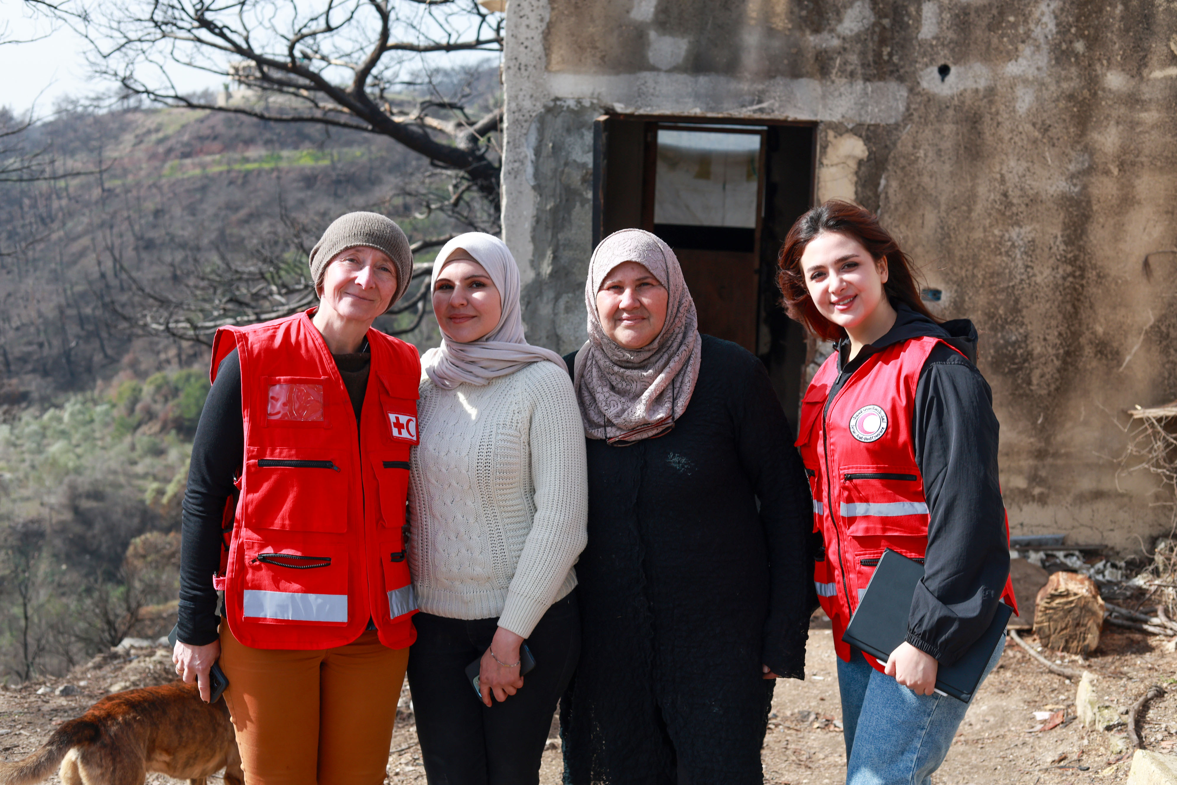 Zwei Rotkreuzhelferinnen mit zwei Frauen vor einem Haus in Syrien