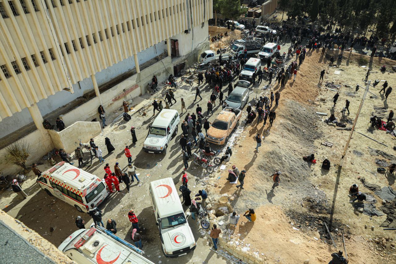 Von oben aufgenommene chaotische Szenen vor Sednaya in Syrien. Mitarbeiter und Autos des Syrisch-Arabischen Roten Halbmond stehen davor.