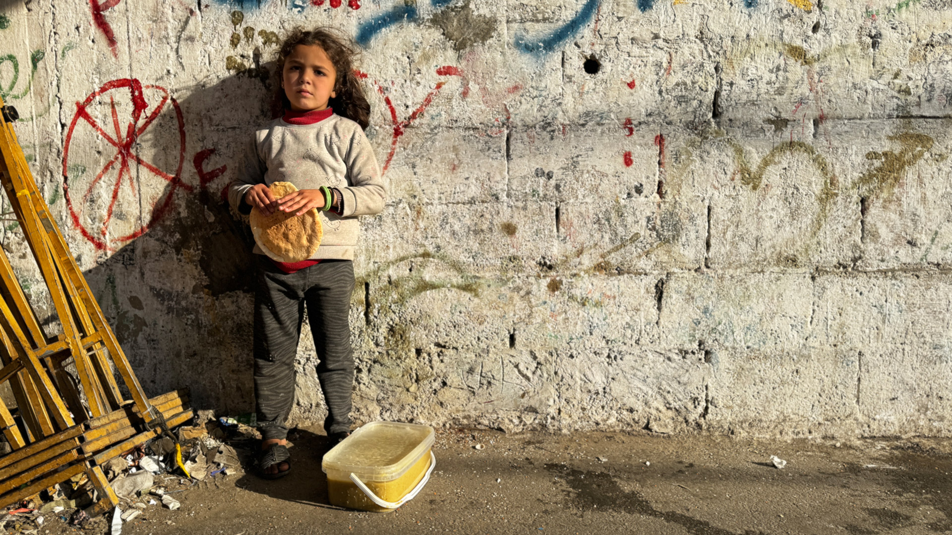 © IKRK / Thomas Glass Mädchen in Gaza steht an einer Wand und hält ein Brot in der Hand