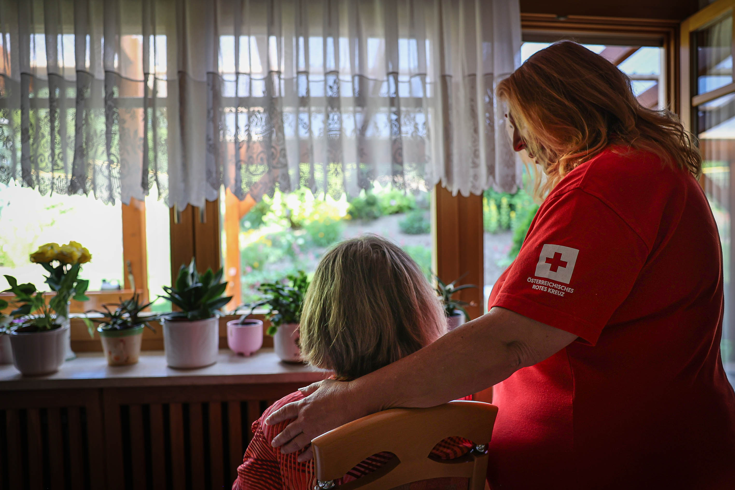 Rotes Kreuz Mitarbeiterin legt Hand auf Schulter einer älteren Frau in Österreich