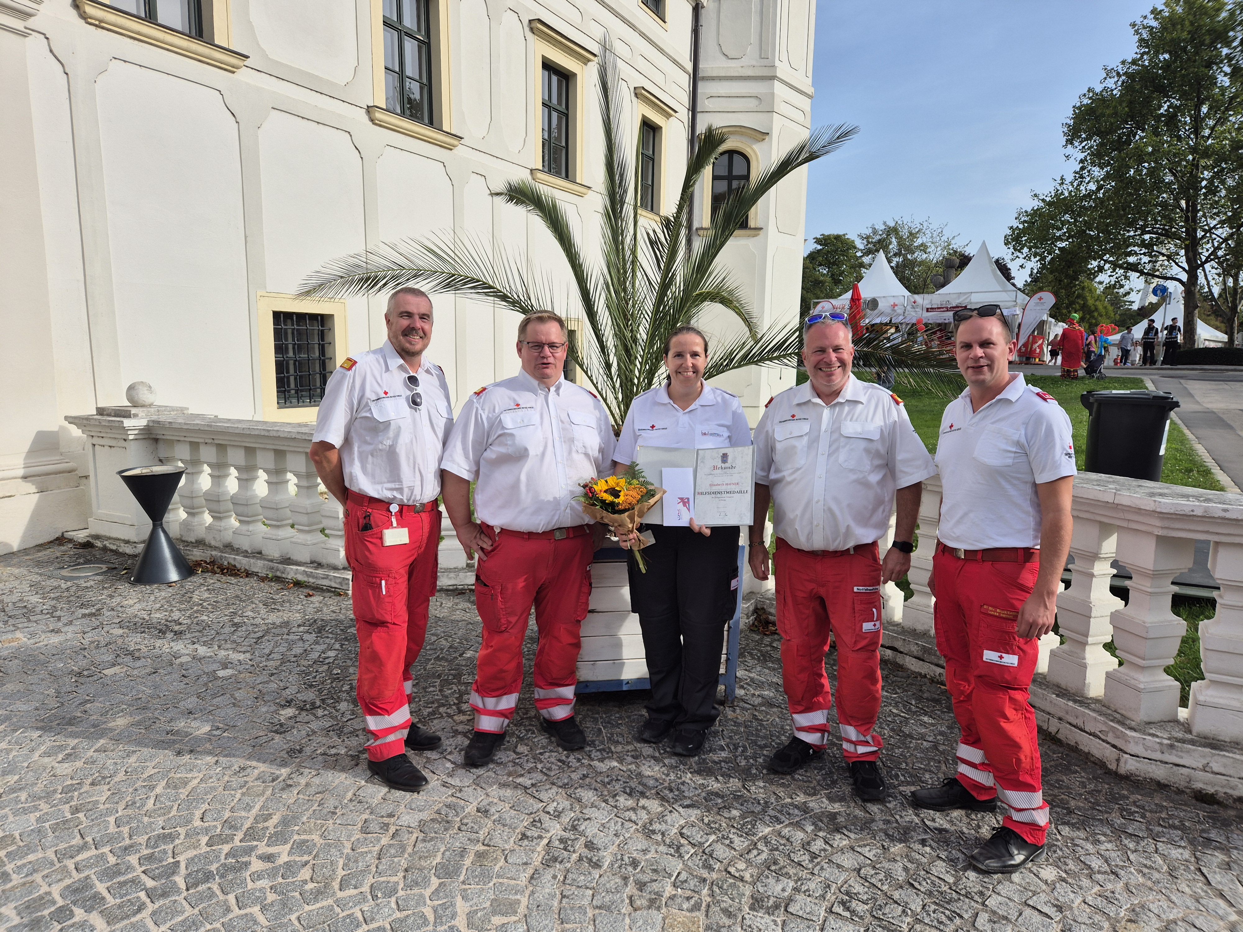 Elisabeth Hafner mit Urkunde, Ehrenzeichen und Blumen gemeinsam mit Kollegen des Roten Kreuzes Schwechat beim Schwechater Stadtfest.
