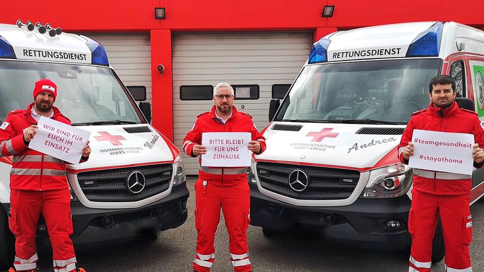 Bitte beleiben Sie daheim - Wir bleiben für Sie im Einsatz - © Rotes Kreuz Sollenau-Felixdorf Drei Sanitäter stehen vor zwei Autos, halten Schilder hoch mit dem Text "Bleibt für uns daheim, wir bleiben für euch im Einsatz!"