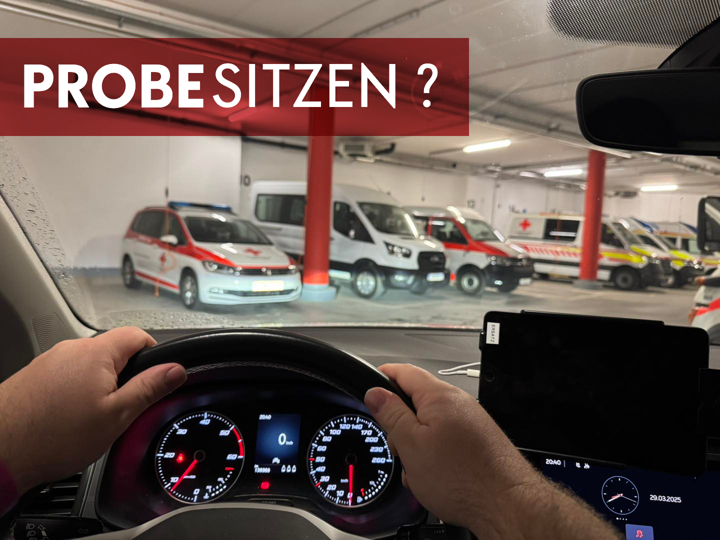 Zwei Hände eines Mitarbeiters am Lenkrad eines BKTWs in der Fahrzeuggarage der Bezirksstelle. Innenaufnahme von der Rücksitzbank, man sieht als das Cockpit und die Hände, sowie in der Windschutzscheibe die Wagenhalle mit Fahrzeugen.