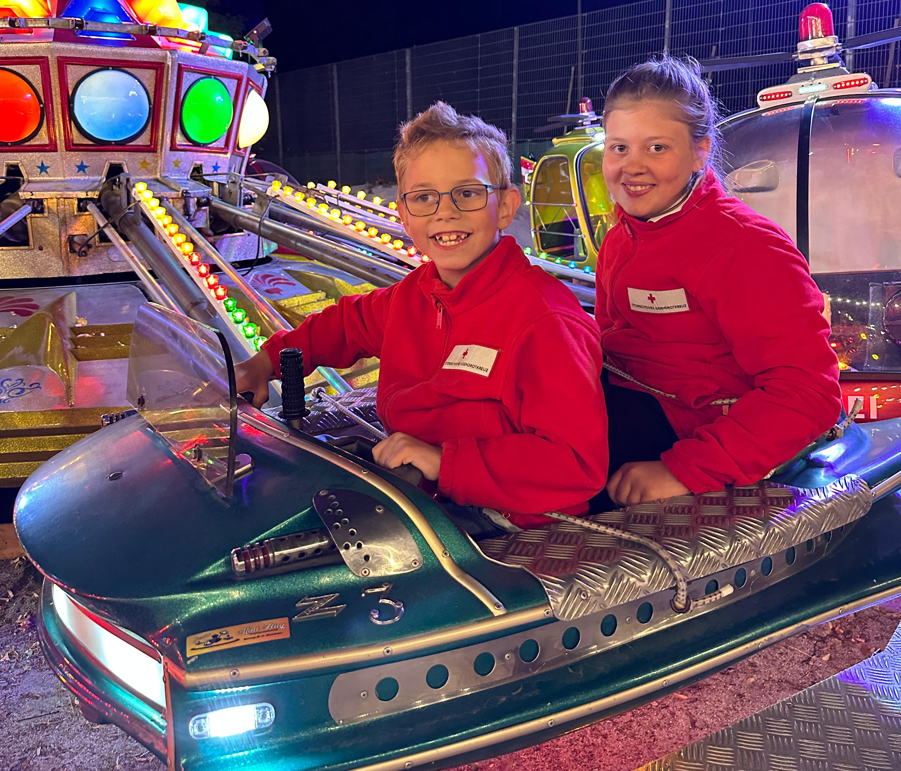 Zwei Jugendrotkreuz-Kinder sitzen glücklich in einem Ringelspiel.