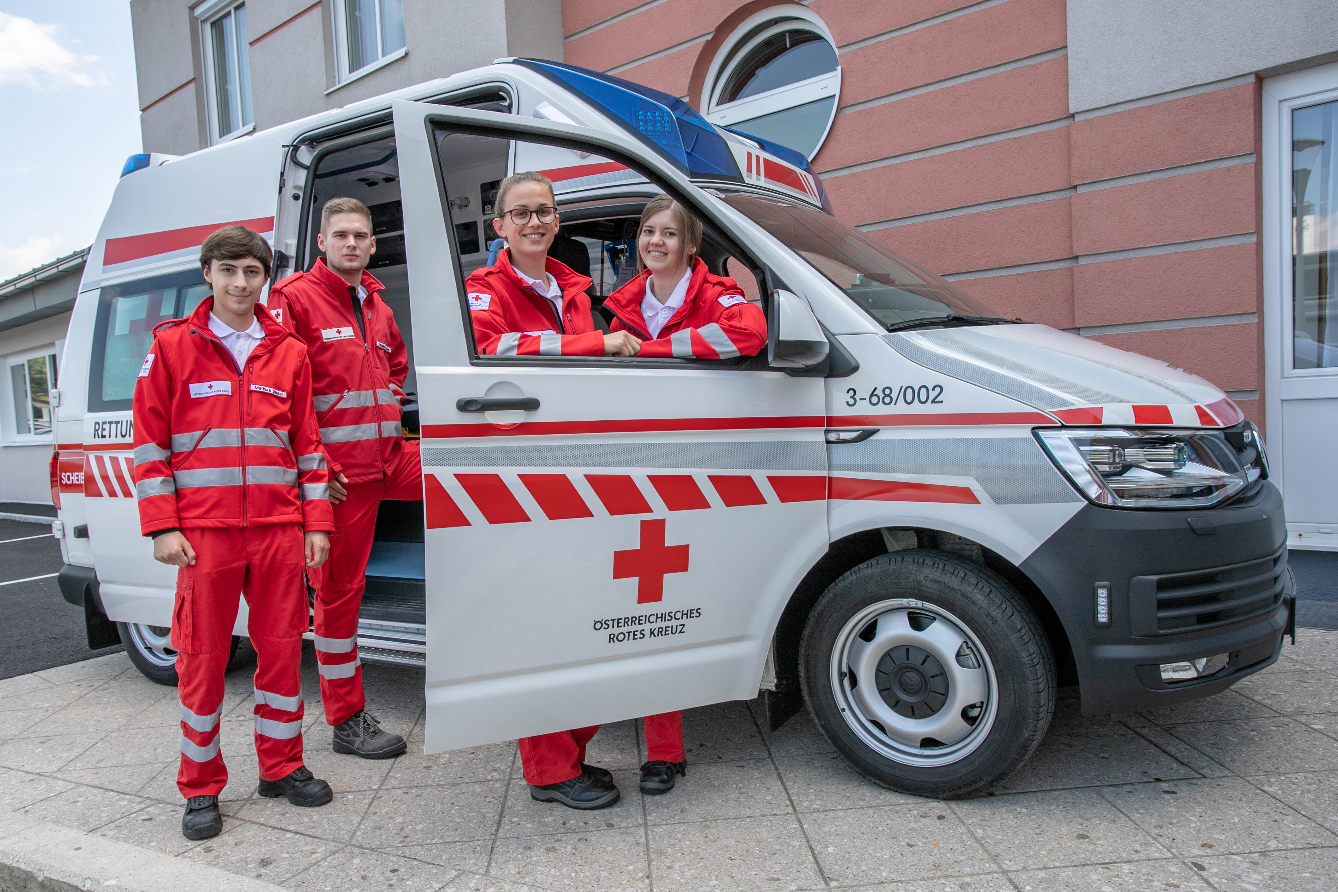 Gruppenfoto junger Menschen vor einem Rotkreuz-Auto