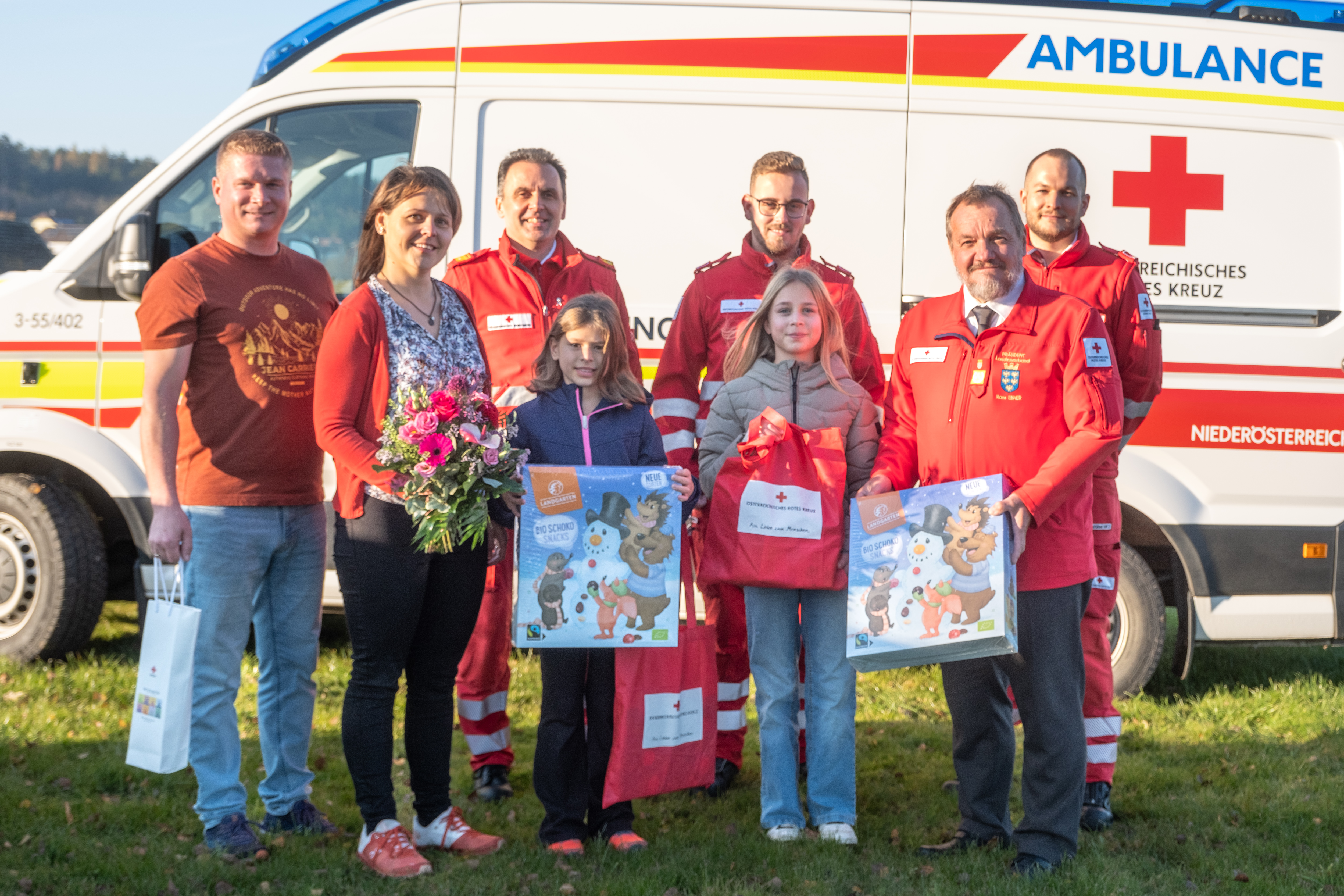 Gruppenfoto der Familie und Rotkreuz-Mitarbeitenden bei der Geschenkübergabe vor dem Rettungsauto
