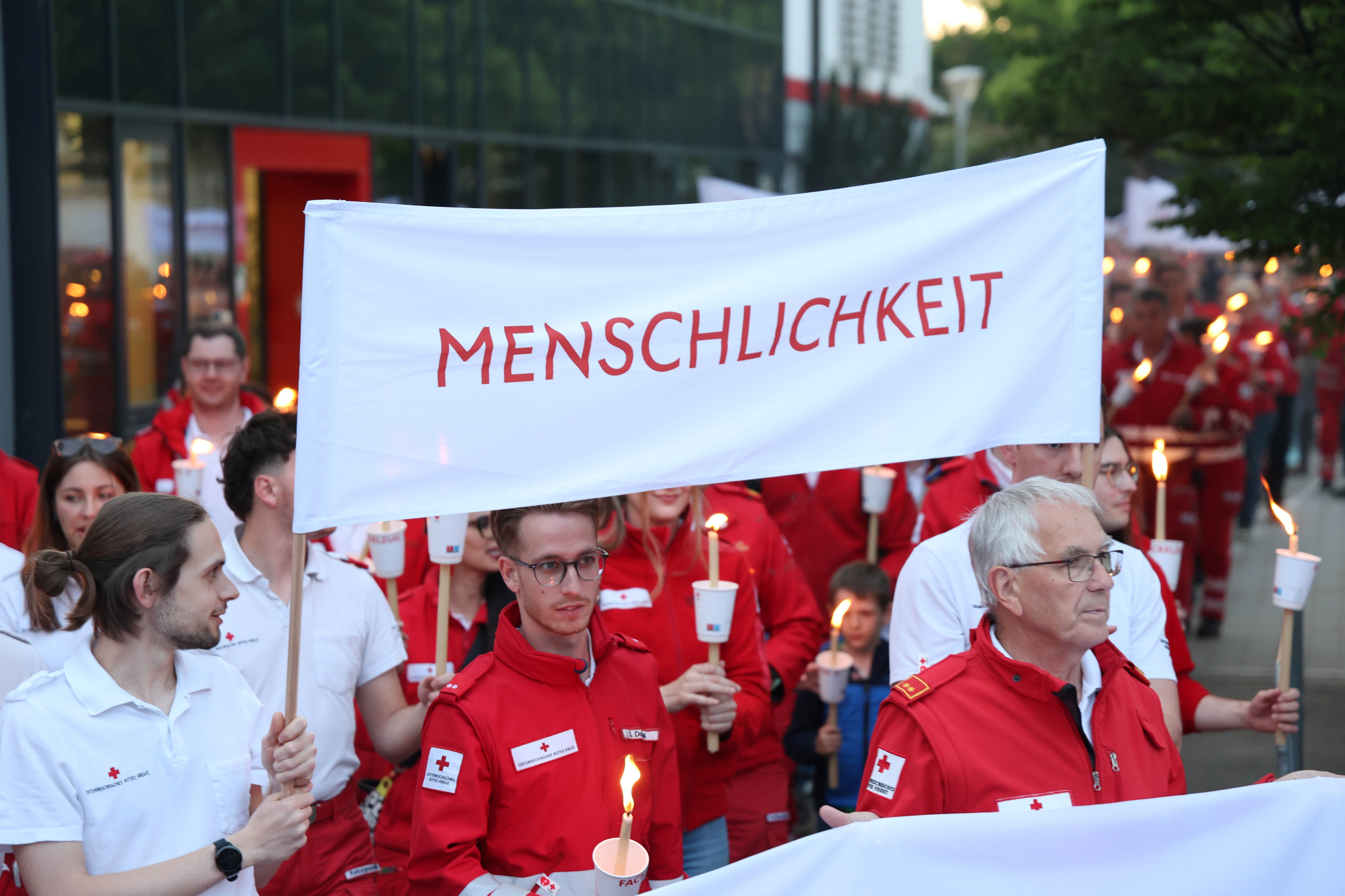 Rotkreuzler:innen tragen ein Banner mit dem Grundsatz "Menschlichkeit"