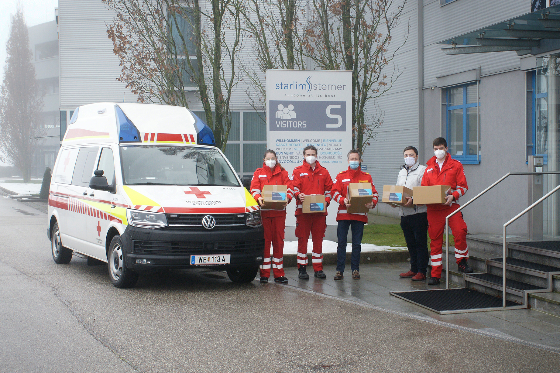 © Starlim Spritzguss GmbH Maskenband-Übergabe mit Dominik Kreuzmayr, Fa. Starlim, Bezirksrettungskommandant Andreas Heinz und Mitarbeiter_innen der Ortsstelle Wels. Vor der Fa. Starlim Sterner mit einem Rettungsauto.