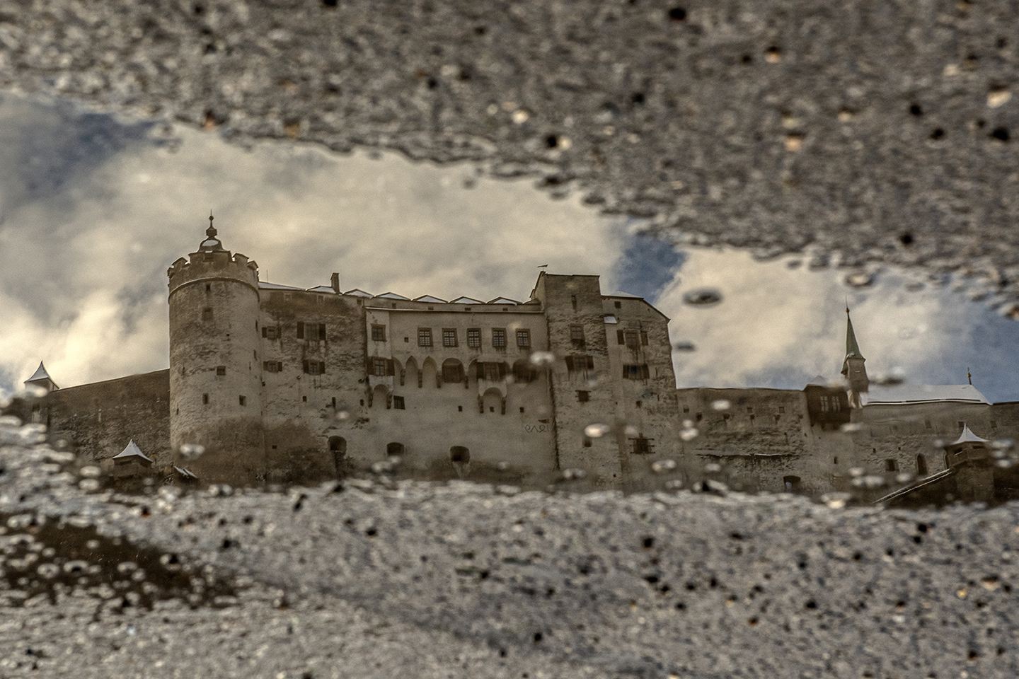 Spiegelung der Festung Hohensalzburg in einer Wasserlacke am Beton