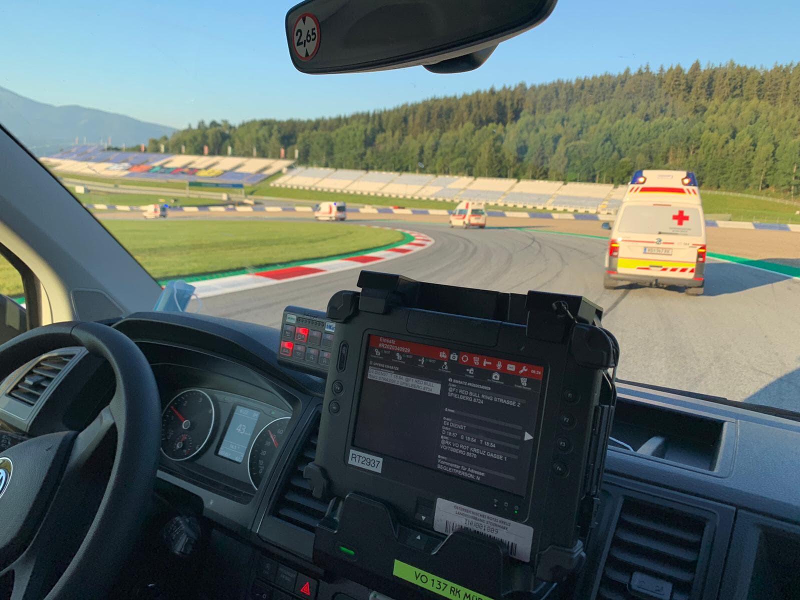 Einige Rettungswagen befinden sich auf einer Rennstrecke (dem Red Bull Ring) und beziehen grade ihre zugewiesenen Posten. Man sieht eine Fahrerkabine von Innen und weitere Rettungswagen vor dem Fahrzeug.