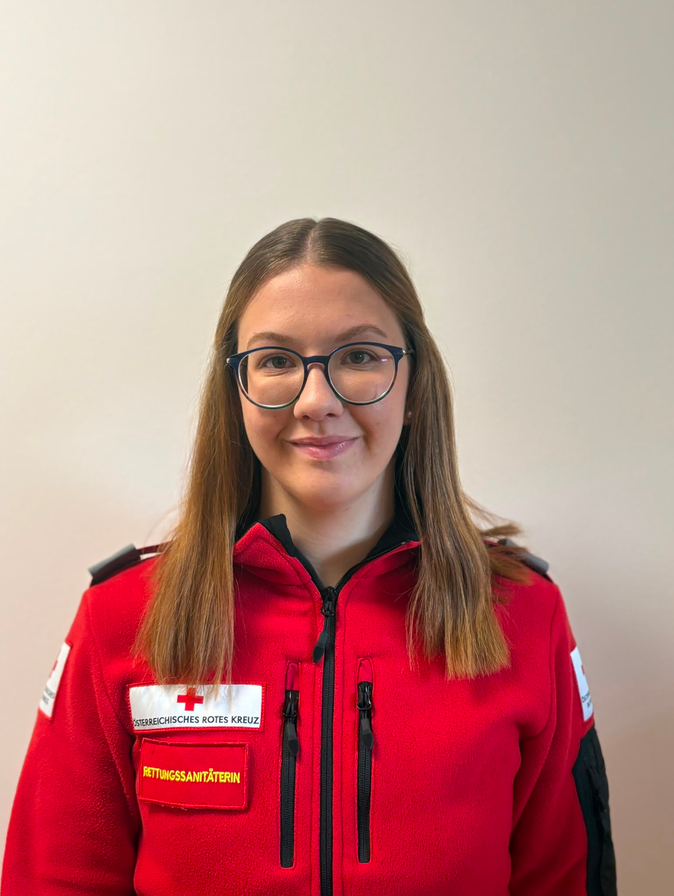 Jasmin Kober in weißem Rotkreuz-Polo vor unscharfem grauen Hintergrund.