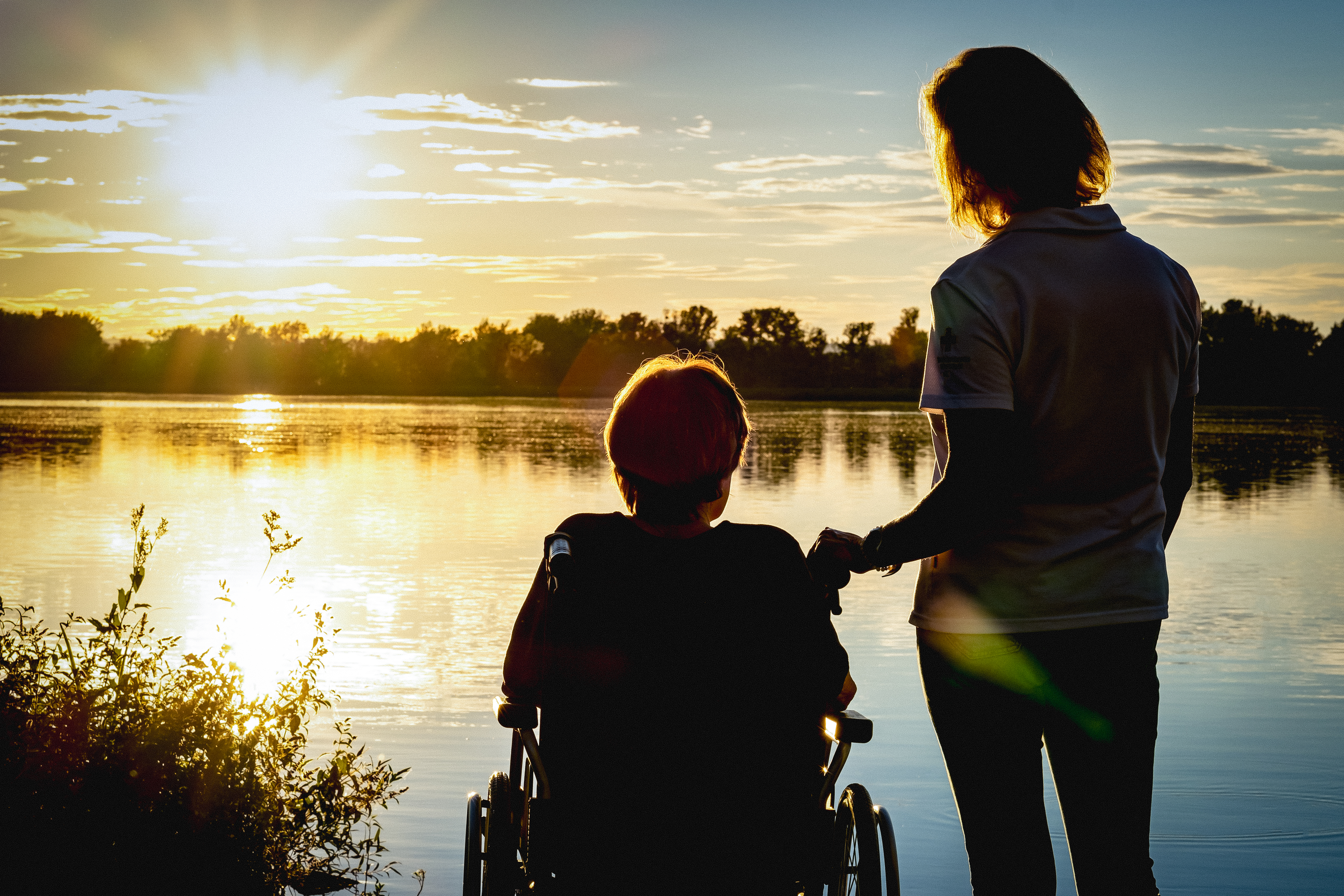 Dame im Rollstuhl mit Rotkreuzmitarbeiterin im Sonnenuntergang