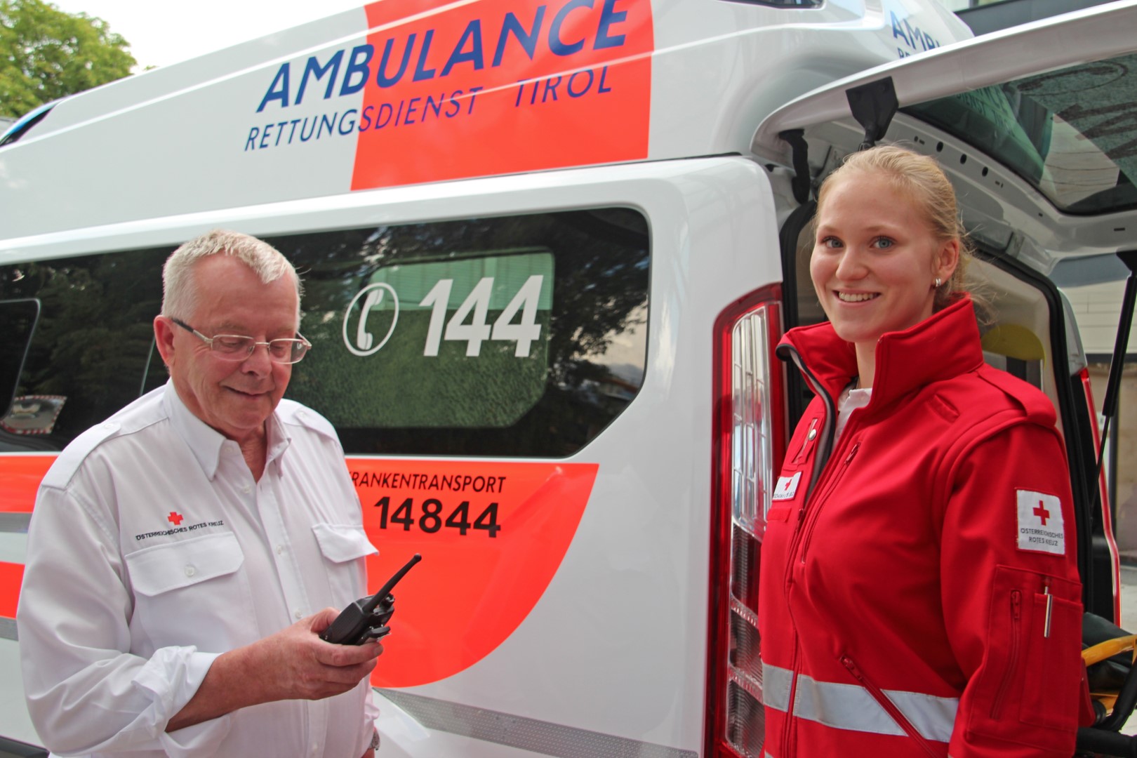 Ein älterer Herr und eine jüngere Frau machen gemeinsam Rettungsdienst. Sie stehen vor einem Rettungsauto